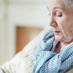 Close-up view of old woman in blue-and-white striped scarf sitting and looking down