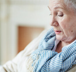 Close-up view of old woman in blue-and-white striped scarf sitting and looking down
