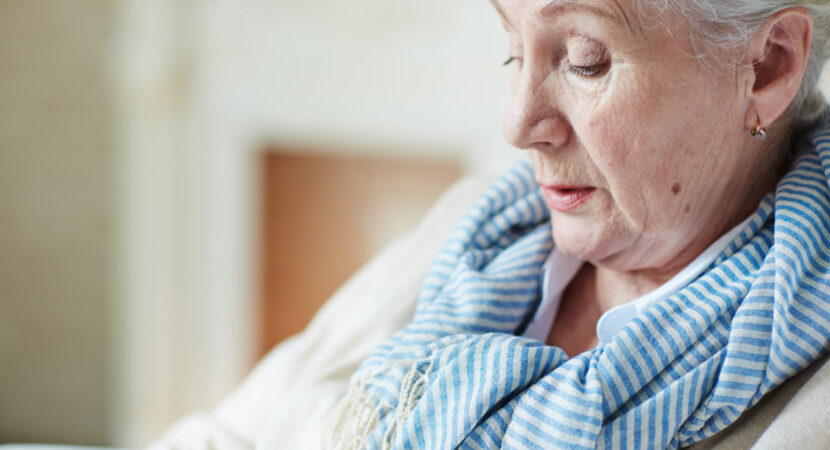 Close-up view of old woman in blue-and-white striped scarf sitting and looking down