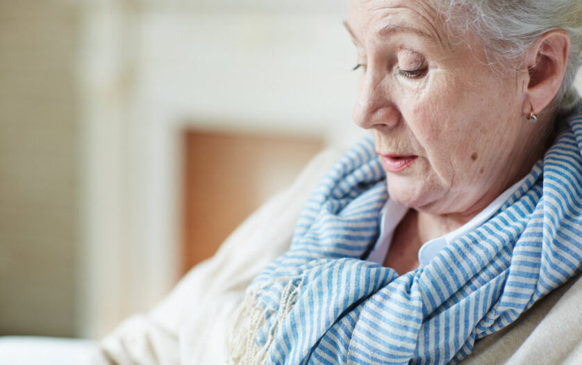 Close-up view of old woman in blue-and-white striped scarf sitting and looking down
