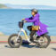 A woman rides an electric bicycle along the waterfront, wearing a purple coat and helmet, on a sunny day.
