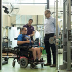 Two sports science professionals working with a girl in a wheelchair in a gym.