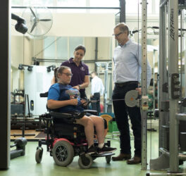 Two sports science professionals working with a girl in a wheelchair in a gym.