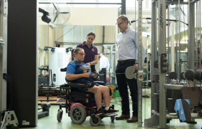 Two sports science professionals working with a girl in a wheelchair in a gym.