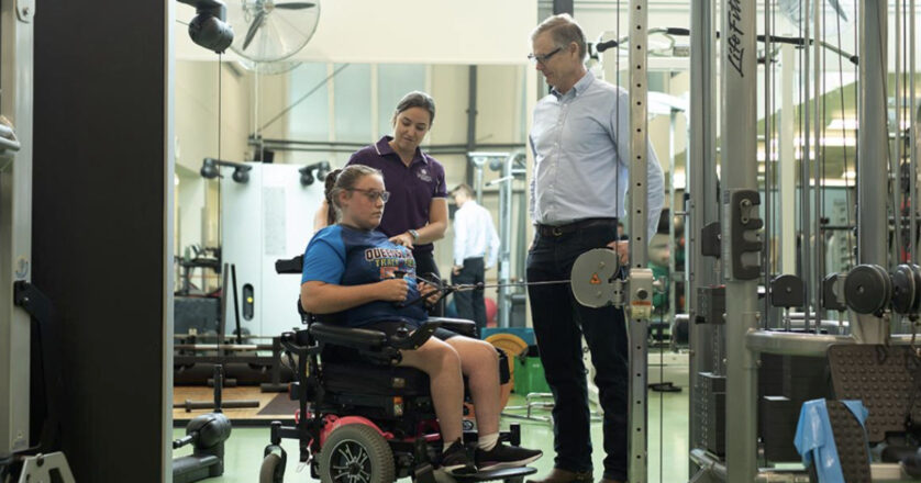 Two sports science professionals working with a girl in a wheelchair in a gym.