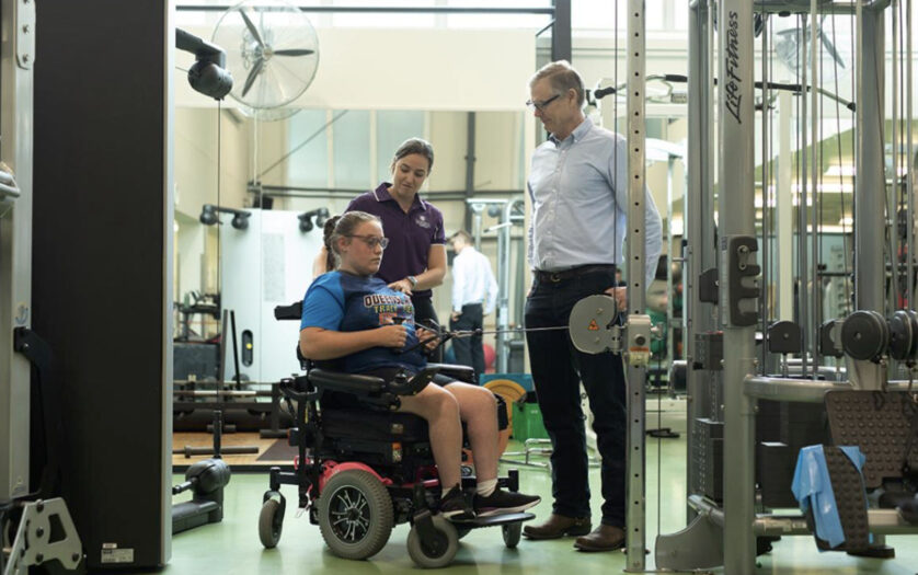 Two sports science professionals working with a girl in a wheelchair in a gym.