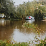 A car struggles through a flooded street surrounded by trees after a heavy rainstorm.