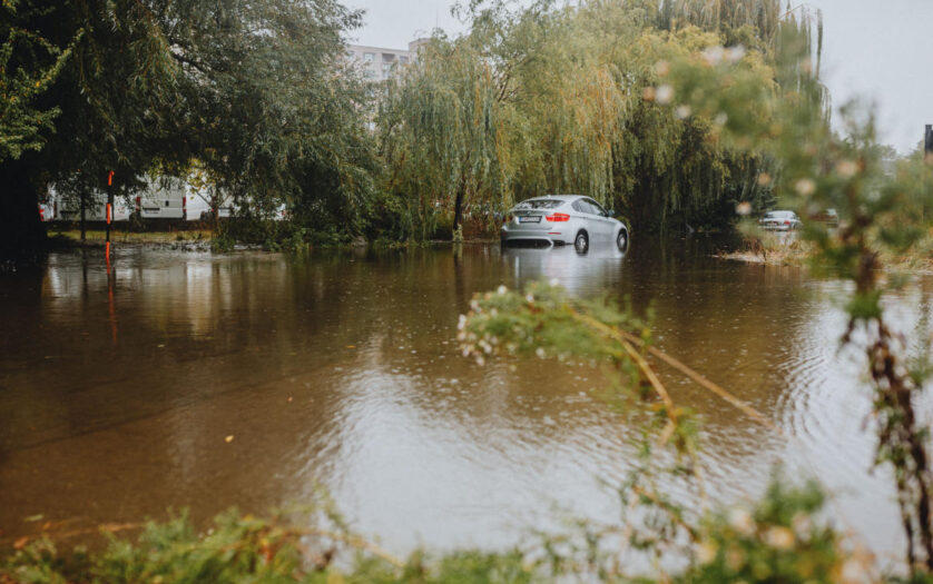 A car struggles through a flooded street surrounded by trees after a heavy rainstorm.