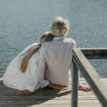 A senior couple enjoys a peaceful moment sitting together on a wooden dock by the lake
