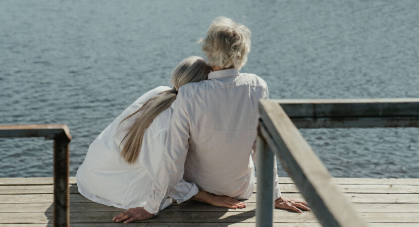 A senior couple enjoys a peaceful moment sitting together on a wooden dock by the lake