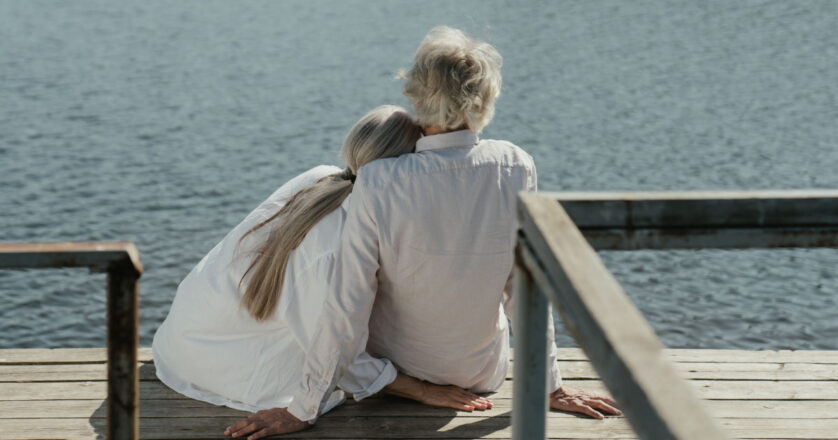 A senior couple enjoys a peaceful moment sitting together on a wooden dock by the lake