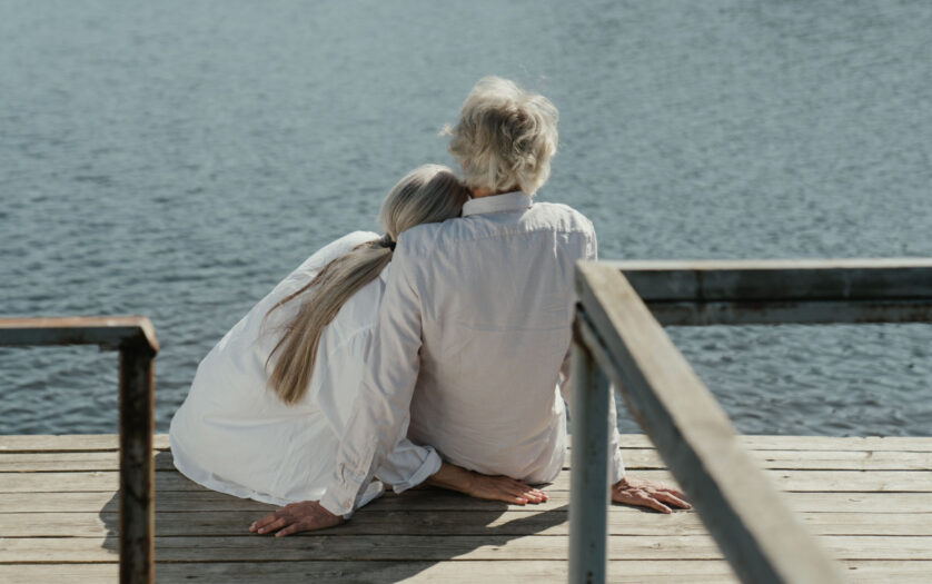 A senior couple enjoys a peaceful moment sitting together on a wooden dock by the lake