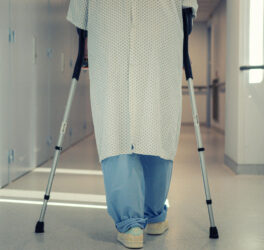 A patient using crutches to walk down a hospital corridor