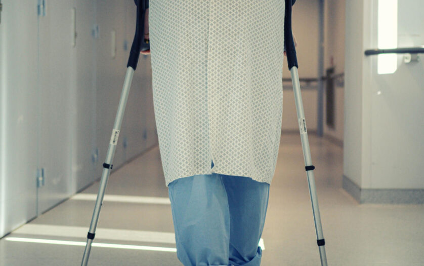 A patient using crutches to walk down a hospital corridor
